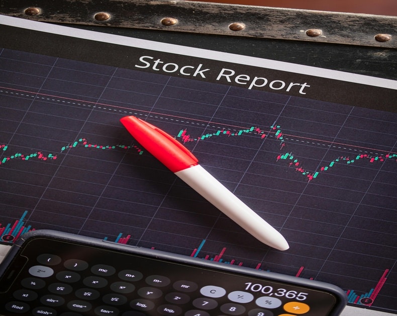 Stock report page showing a candlestick stock chart with a red-and-white pen and a calculator below.