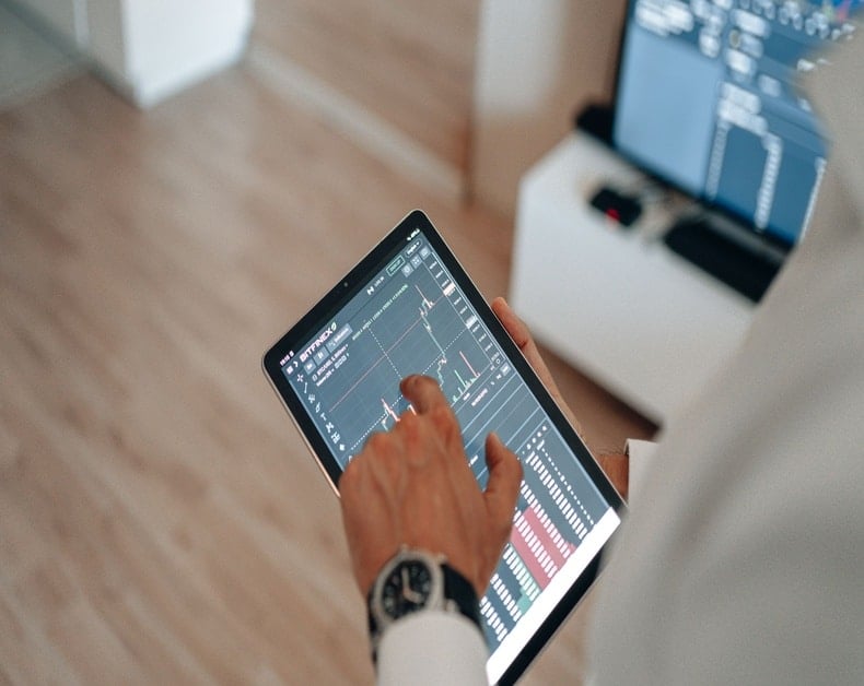 Person in white shirt and watch uses a tablet showing a financial chart and market data.