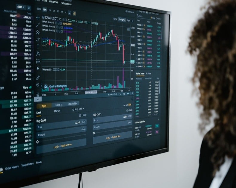Trading dashboard on a monitor showing candlestick chart, volume bars, and market data for stocks or crypto equilibrium.